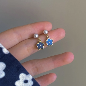 Pendientes de perlas con colgante de flor azul y borde dorado sostenidos a mano