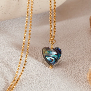 Detailed close-up of heart-shaped abalone shell pendant on a golden ball chain necklace