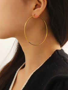 Macro side view of a large polished 18K gold stainless steel hoop earring on a model
