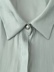 Detail of light green satin shirt featuring a classic collar and silver metal button