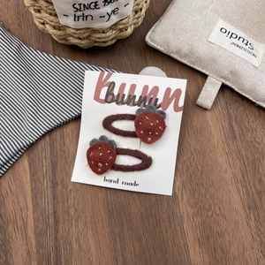 Detail of cute handmade strawberry hair clips with red plush texture and brown base
