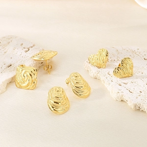 Macro shot of three pairs of gold geometric earrings with spiral textured finish on white stone