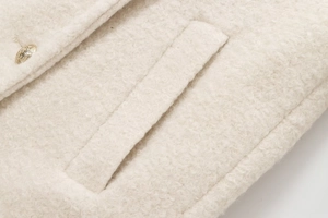 Detail of cream bouclé fabric showing the texture and a gold embossed button