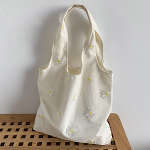 Detailed embroidery of white and yellow daisies on cream canvas shopping bag texture