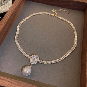 Detail of gold plated necklace with a large white pearl pendant and zircon stones
