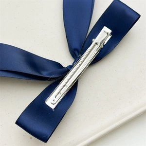 Detail of the silver metal duckbill clip with anti-slip teeth on a navy ribbon bow