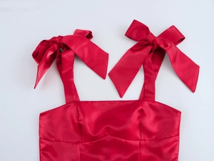 Détail de la robe en satin rouge avec bretelles à gros nœuds et décolleté carré élégant