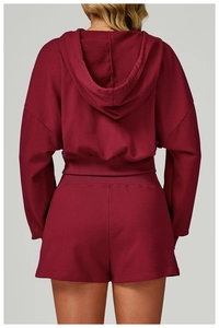 Back view of women's burgundy cropped zip hoodie and matching shorts set in studio setting