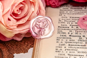 Detail of pink wax seal stickers with embossed heart and bow on vintage book backdrop