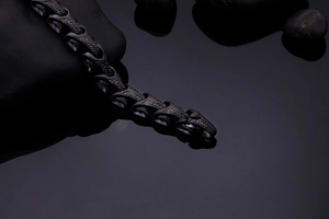 Gros plan d'un bracelet gourmette noire style dragon sur fond de pierre sombre