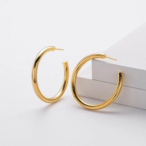 Detail van de gepolijste gouden buisvormige C-oorringen op witte geometrische blokken