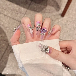 Handgemaakte kunstnagels met paarse hartstenen, zilveren strikjes en parels op een verloop