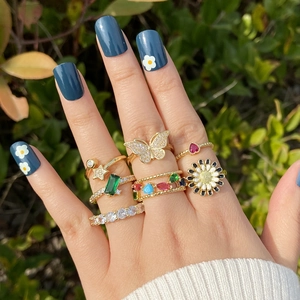 Golden ring set with butterfly and daisy motifs on a model's hand in sunlight