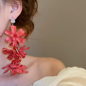 Detail of model wearing long red fabric flower tassel earrings with square crystal studs