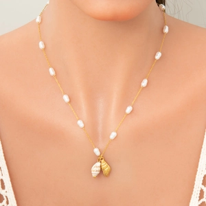 Close-up of golden pearl necklace with double shell pendants worn by a female model