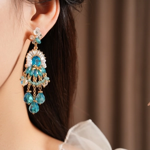 Dettaglio di orecchini vintage con nappine blu e perle indossati da una modella elegante