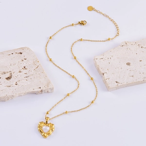 Gold heart pearl necklace with textured edges and beads on a minimalist white background