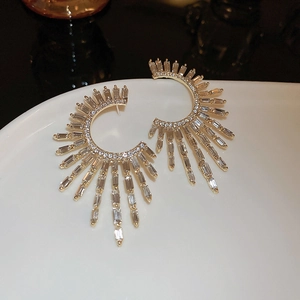 Macro shot of gold C-shaped earrings with radiating rectangular zircons on a white plate