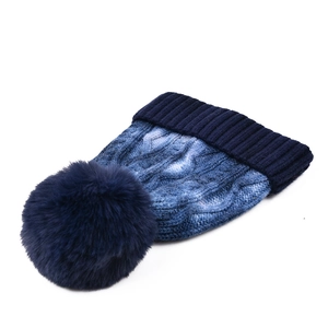 Close-up of tie-dye knit beanie with navy blue faux fur pompom and ribbed cuff detail