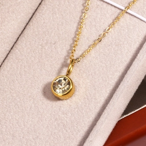 Detailed macro shot of a gold birthstone necklace with a round clear crystal pendant