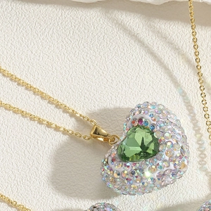 Macro shot of gold heart pendant with green gemstone and rainbow pave setting