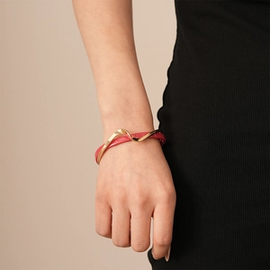 Detail of a wave-patterned gold-plated bangle with red enamel finish on a model's wrist