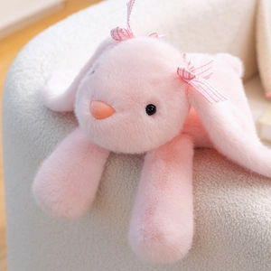 Peluche lapin rose aux longues oreilles avec nœud à carreaux sur un canapé blanc