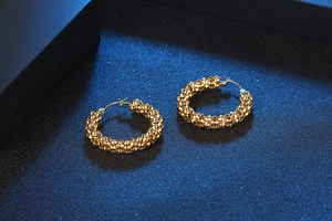 Macro detail of gold hoop earrings with distinctive textured granulated surface on blue