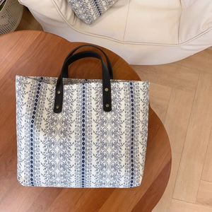 Floral cotton tote bag with blue patterns and black leather handles on a wooden table