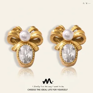 Close-up of golden bow earrings featuring white pearl and oval gemstone detail