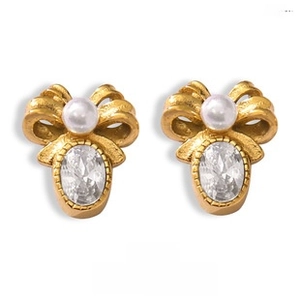 Close-up of golden bow earrings featuring white pearl and oval gemstone detail