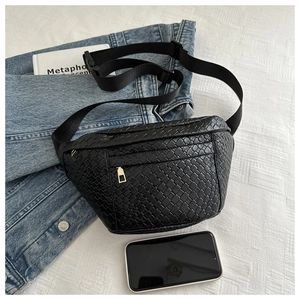 Detail of black woven waist bag with gold zipper shown against denim and white bedding