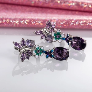 Silver oval purple zircon flower earrings with butterfly accents on reflective surface