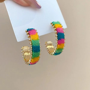 Close-up of bohemian C-shaped earrings with colorful knit stripes and golden bead trim
