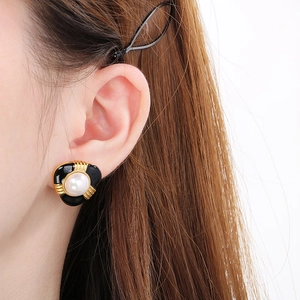 Close-up of a French style gold stud earring with black enamel and central pearl on model