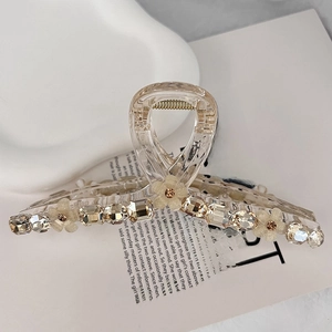 Close-up of a clear hair claw clip decorated with crystals and small flowers on white paper