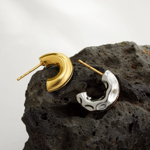 Detailed close-up of gold smooth and silver hammered C-shaped earrings on black volcanic rock