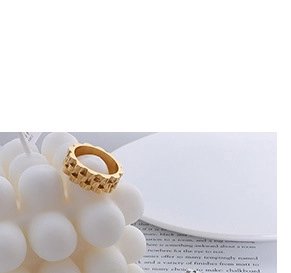 Detail shot of golden pyramid-studded geometric ring on white candle and magazine background