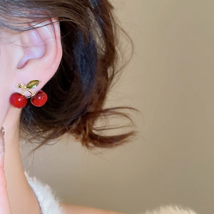 Detail view of red cherry earrings with green crystals and gold finish on model