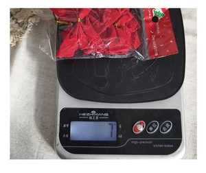 Close-up of twelve red Christmas tree bows in packaging being weighed on a digital scale