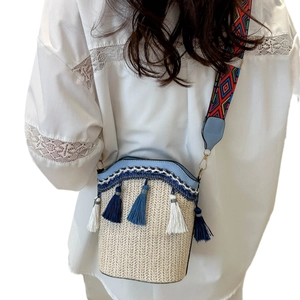 Woven straw bucket bag with blue tassels and colorful geometric patterned shoulder strap