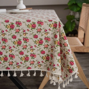 Detailed macro view of beige linen tablecloth with red floral pattern and white tassels