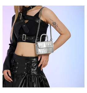 Model showcasing a small silver embossed patent leather bag with a metal chain strap