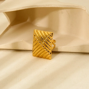 Macro detail of rectangle textured 18K gold plated stainless steel ring on beige fabric