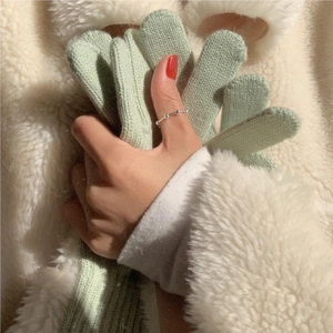 Close-up of light green knitted winter gloves on a soft white lamb wool background