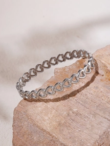 Close-up of hollow heart pattern silver steel bangle displayed on natural stone texture