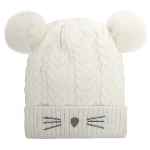 Detail of white knit baby beanie with cable stitch, plush pom-poms, and cat embroidery