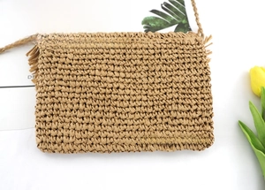 Detail of hand-woven straw crossbody bag with decorative fringe on a tropical backdrop