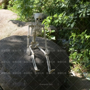 Realistic white plastic human skeleton model sitting on a rock for Halloween garden decor