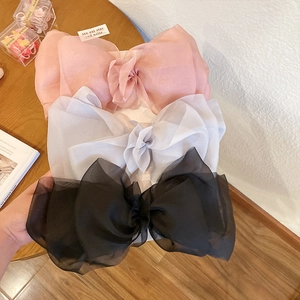 Three elegant organza bow hair claws in pink, white, and black on a wooden surface